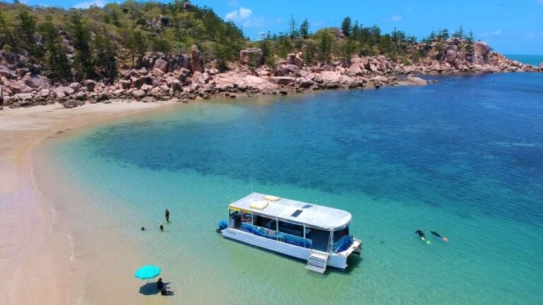 A little boat laying in a bay of clear water with people snorkeling and swimming around.