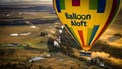 A hot hair balloon from Balloon Aloft flying above the country side.