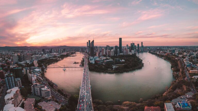 Brisbane skyline at sunset with pink hues, overlooking the Brisbane River.