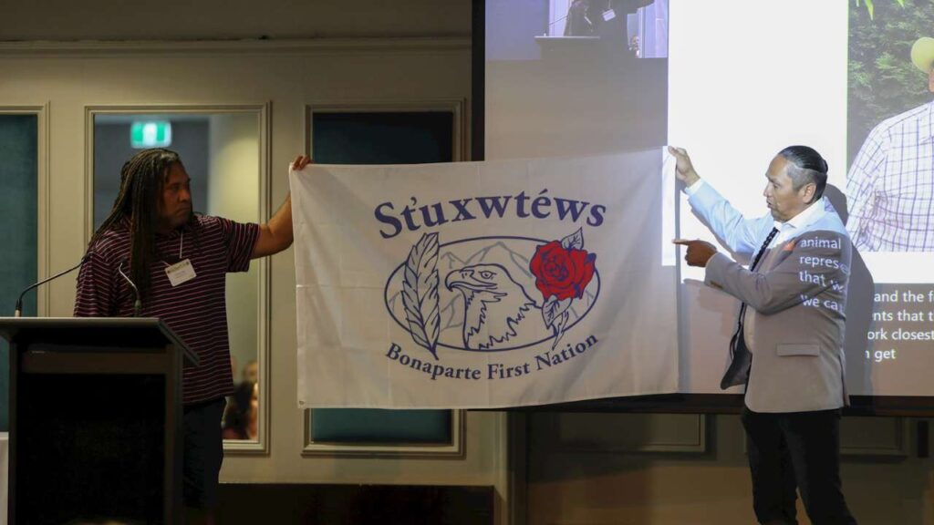 Chief Frank Antoine, Bonaparte First Nation Chief, (right) explains the symbols on the St'uxwtews flag, which was later gifted to Fraser Nai (Strait Experiences; left).
