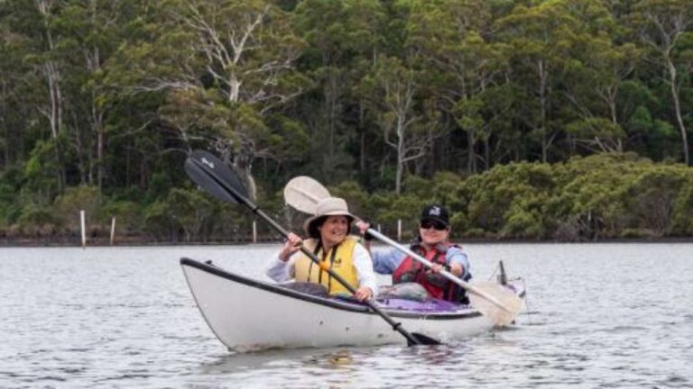 Two people in a canoe on a lake, surrounded by mountains and trees