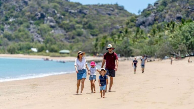 Family walking along a beach in Townsville with mountains in the backdrop.